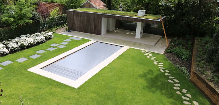 Poolhouse met een plat sedumdak achter een zwembad en een gazon met stapstenen